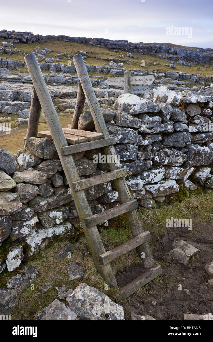 Un stile di legno su un muro di pietra nel Yorkshire Dales adiacente ad un segno per la Pennine Way al Malham Cove Foto Stock