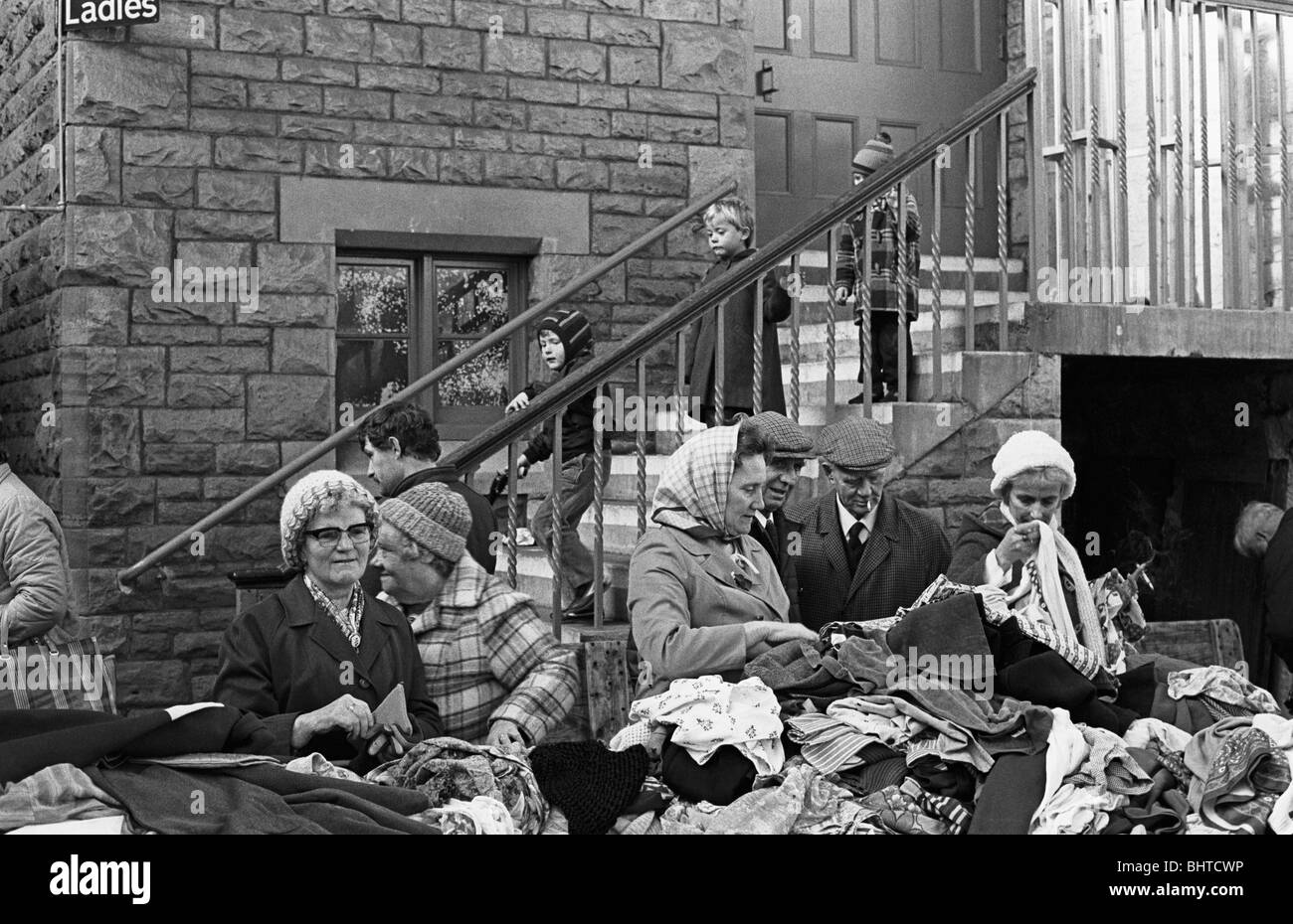 Gratuita per tutti come i pensionati anziani setacciare attraverso pile di capi di abbigliamento esterno sinistro per una comunità hall. Foto Stock