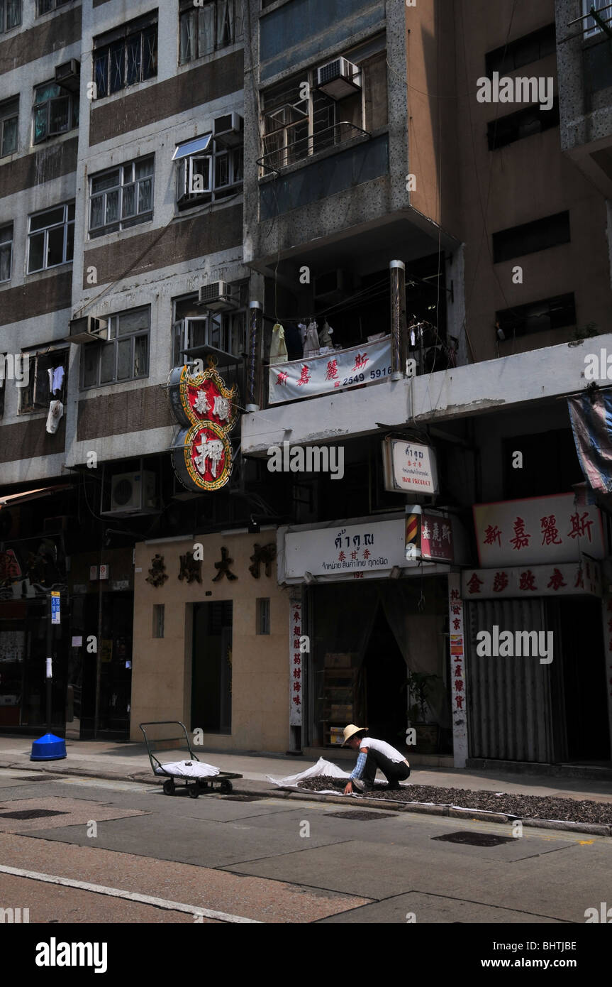 Ritratto di una donna in un bambù hat diffusione di frutti di mare al sole su un marciapiede fuori casa negozi, Queen's Road West, Hong Kong Foto Stock