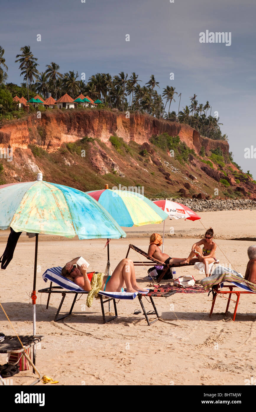 India Kerala, Varkala Beach, western i visitatori a prendere il sole sotto colorati ombrelloni da spiaggia Foto Stock