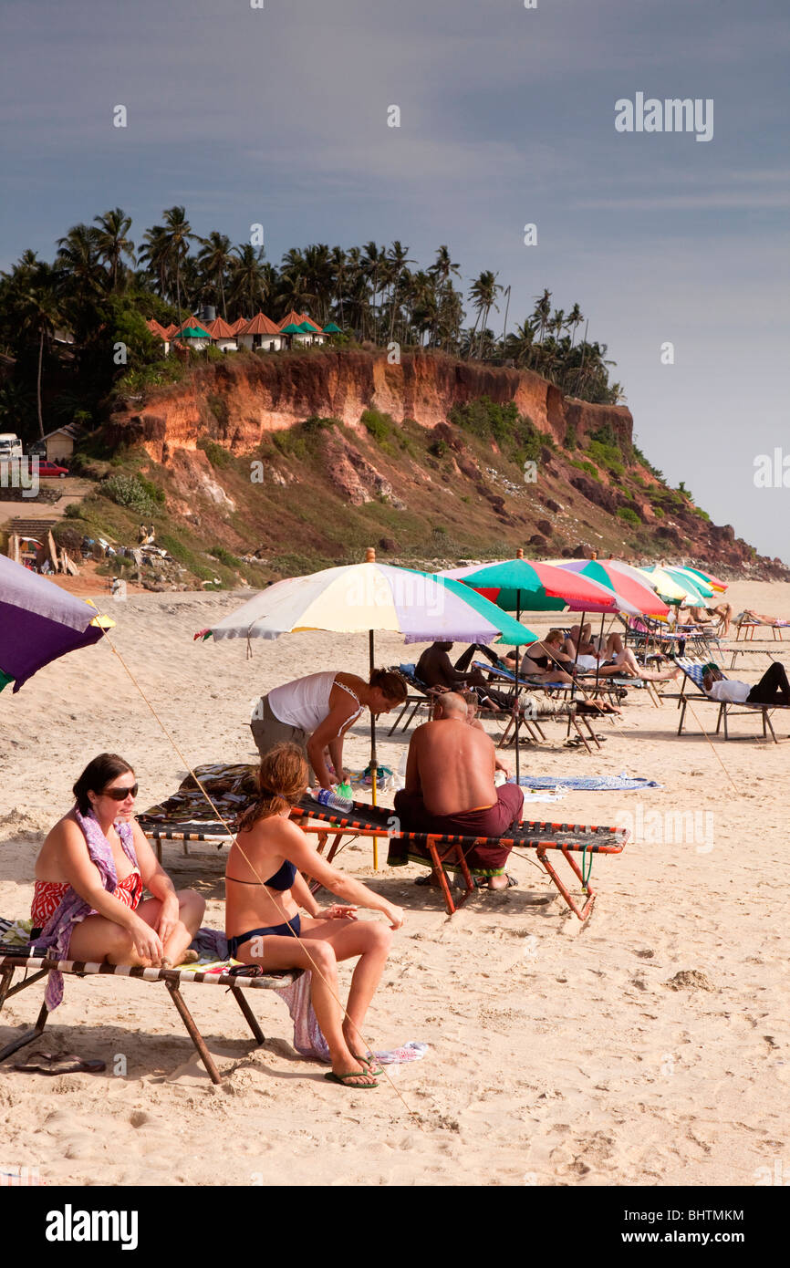 India Kerala, Varkala Beach, western i visitatori a prendere il sole sotto colorati ombrelloni da spiaggia Foto Stock