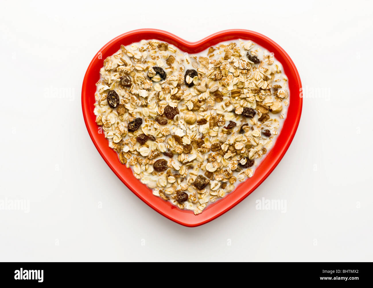 Studio shot di rosso a forma di cuore ad una ciotola di muesli e latte su uno sfondo bianco, ripresa dall'alto. Foto Stock