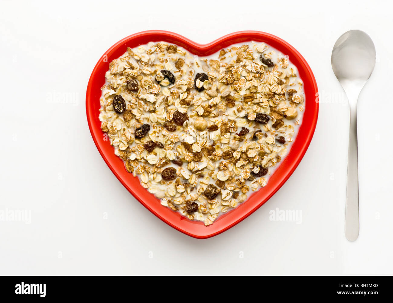 Studio shot di rosso a forma di cuore ad una ciotola di muesli e latte su uno sfondo bianco, ripresa dall'alto. Foto Stock