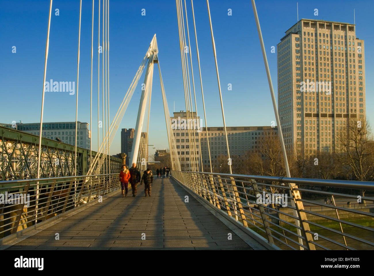 La gente camminare lungo il Golden Jubilee Bridge di Londra centrale con il guscio edificio in background. Foto Stock