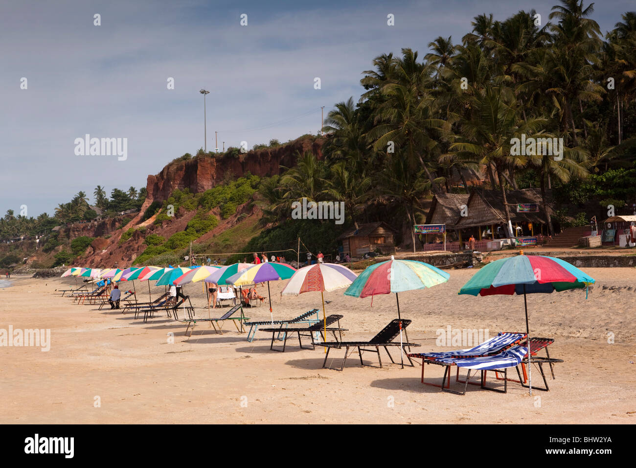 India Kerala, Varkala Beach, colorati ombrelloni e sdraio vuota sotto le scogliere Foto Stock