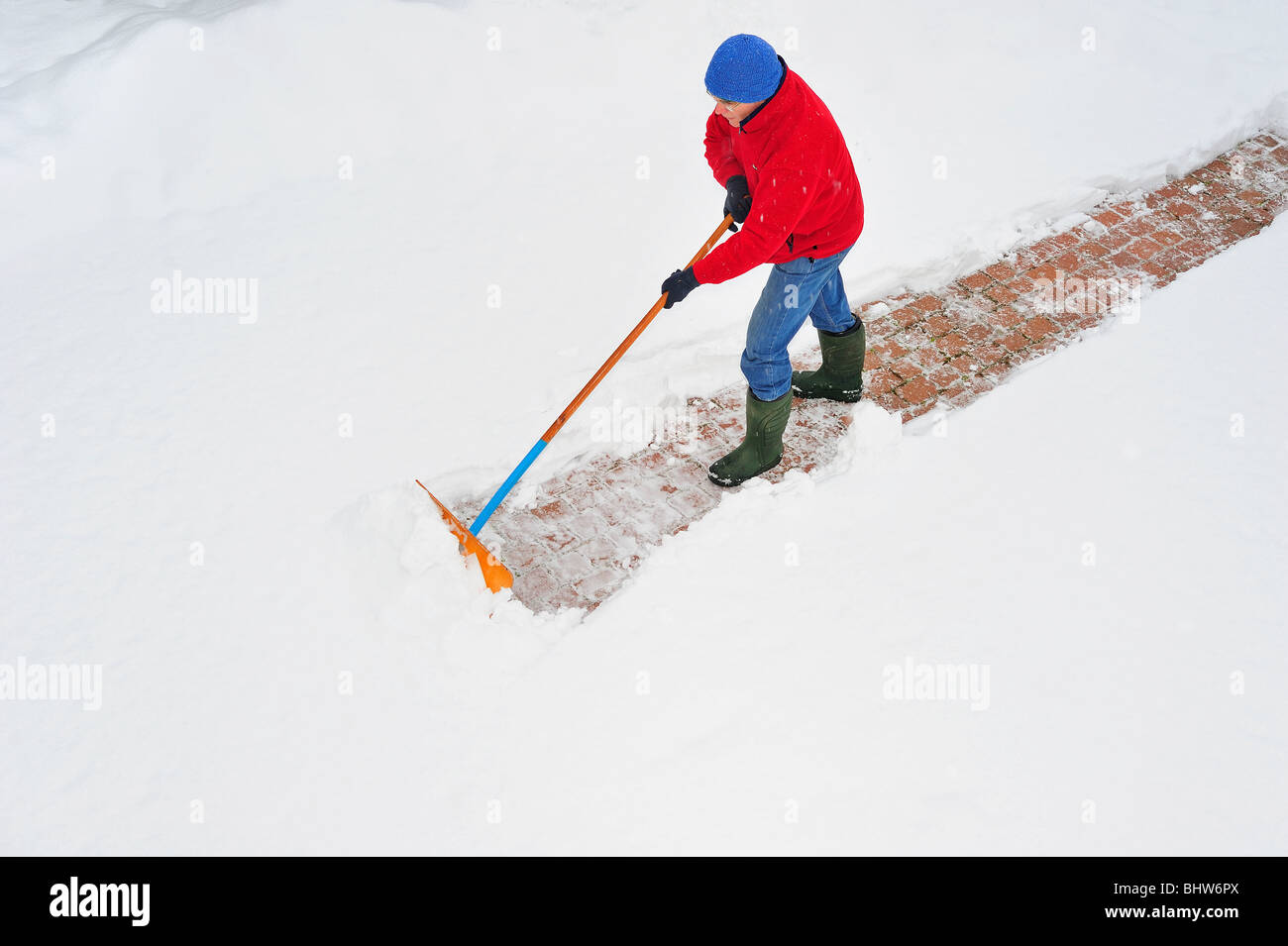 Un uomo spalare la neve dal suo passo carraio nevoso, presa da un punto di vista di alta. Ancora neve caduta. Spazio per il testo sulla neve. Foto Stock