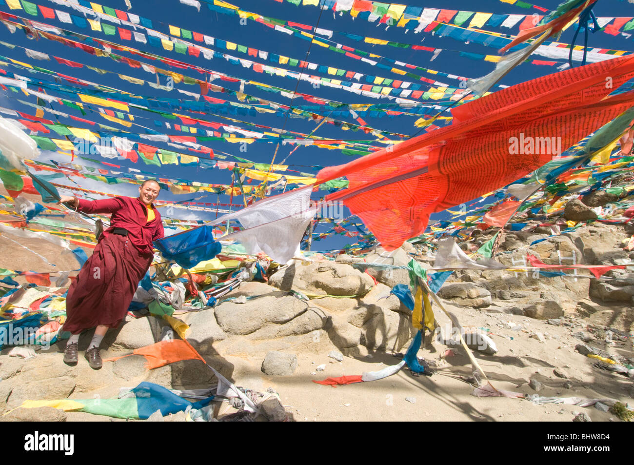 Un monaco buddista in piedi accanto alle bandiere di preghiera in Tibet Foto Stock