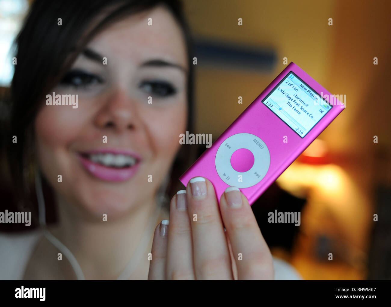 Giovane donna in un momento di relax a casa ascoltando musica su un Apple iPod nano rosa dispositivo di storage Foto Stock