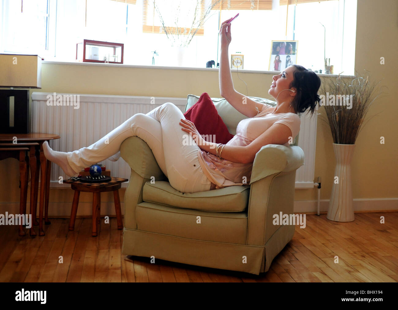 Giovane donna in un momento di relax a casa ascoltando musica su un Apple iPod nano rosa dispositivo di storage Foto Stock