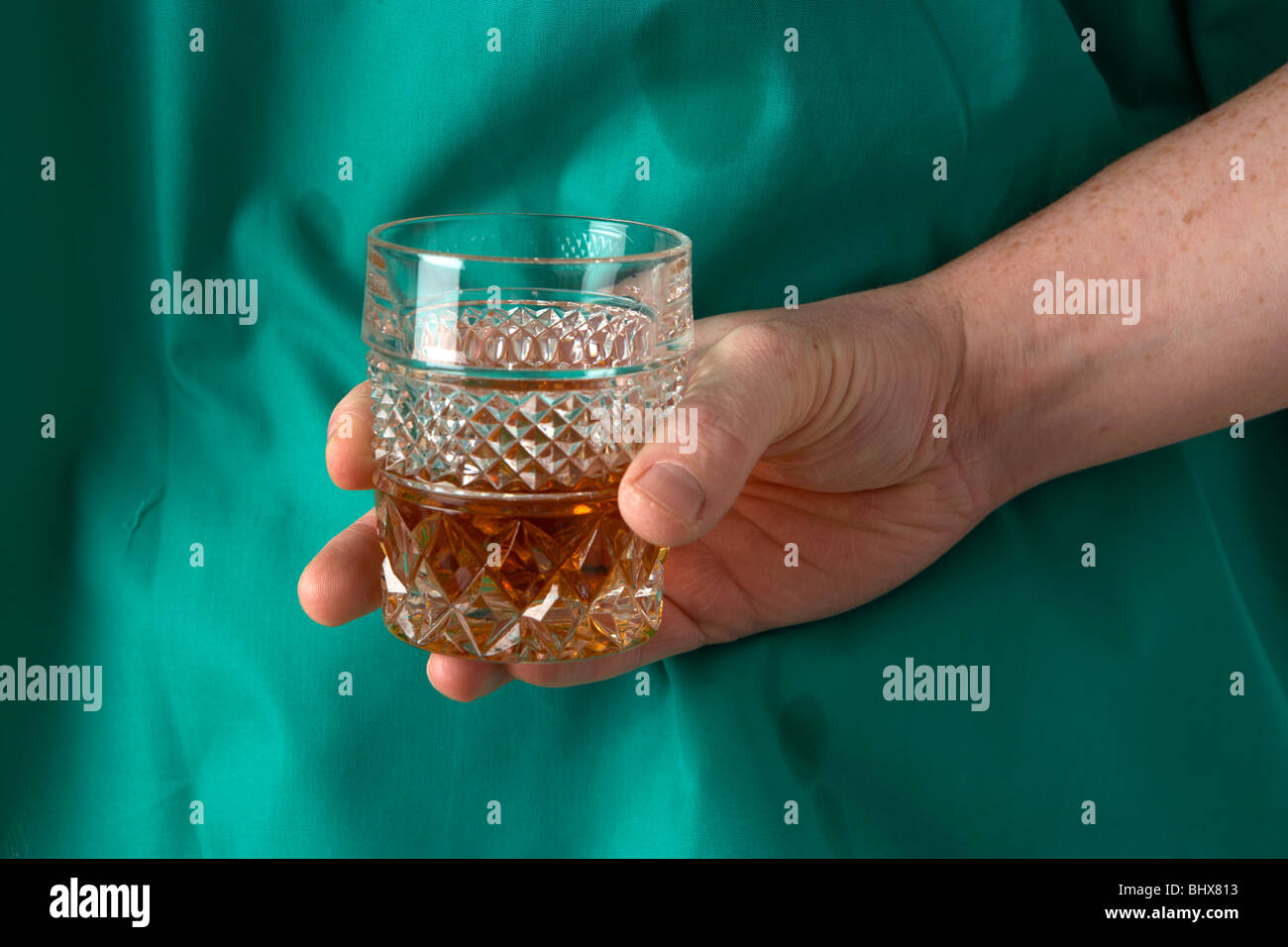 Uomo che indossa medical scrubs tenendo un bicchiere di liquori alcol dietro la schiena Foto Stock