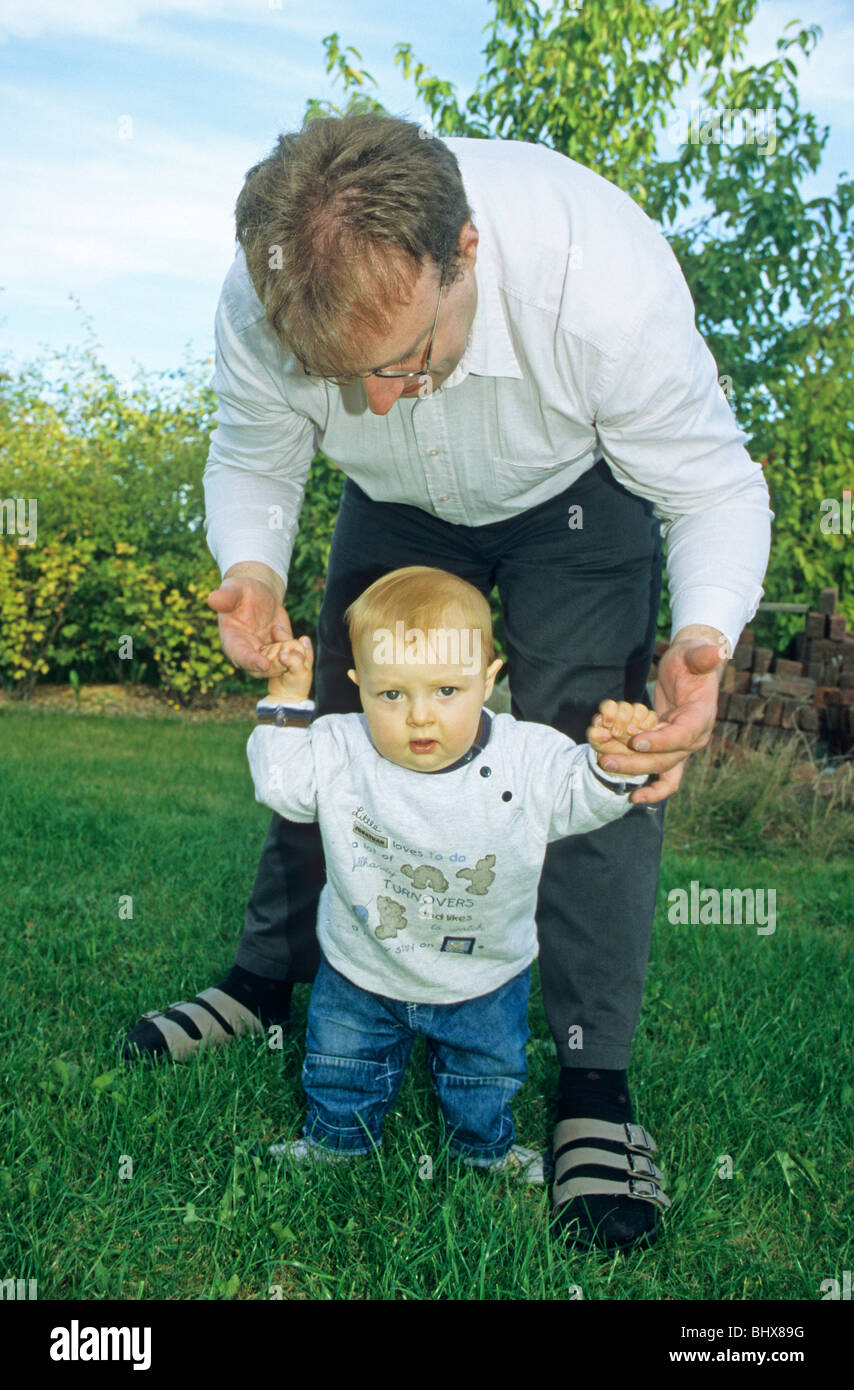 Un giovane padre aiutando il suo Figlio bambino a camminare Foto Stock