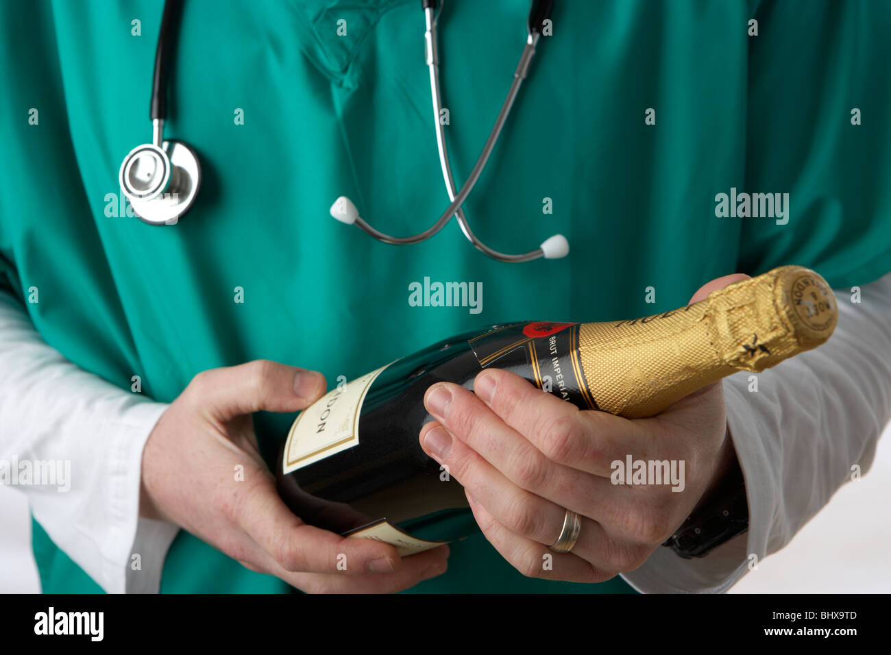 Uomo che indossa medical scrubs e stetoscopio tenendo la bottiglia di champagne Foto Stock