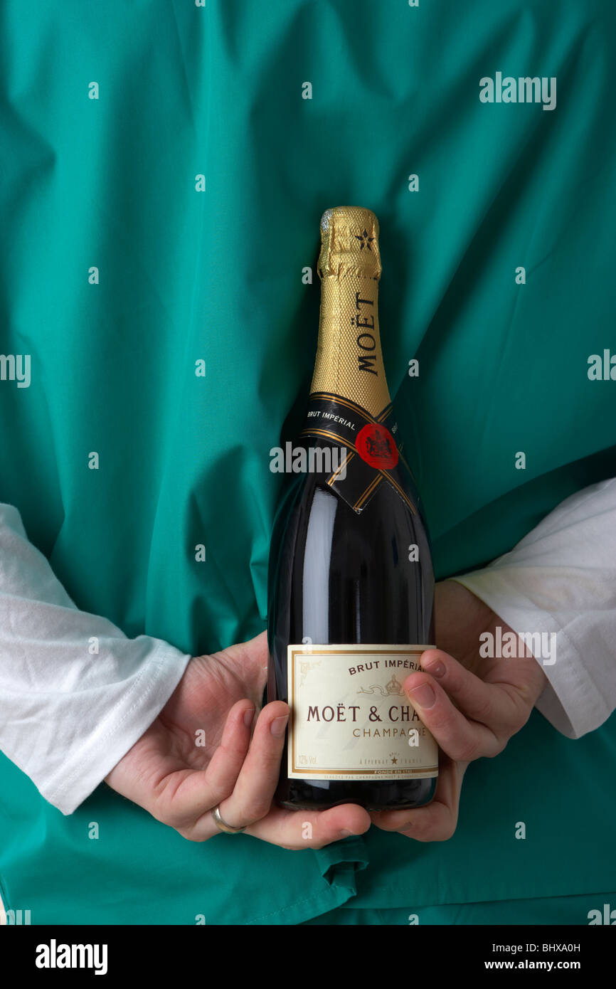 Uomo che indossa medical scrubs tenendo la bottiglia di champagne dietro la schiena Foto Stock
