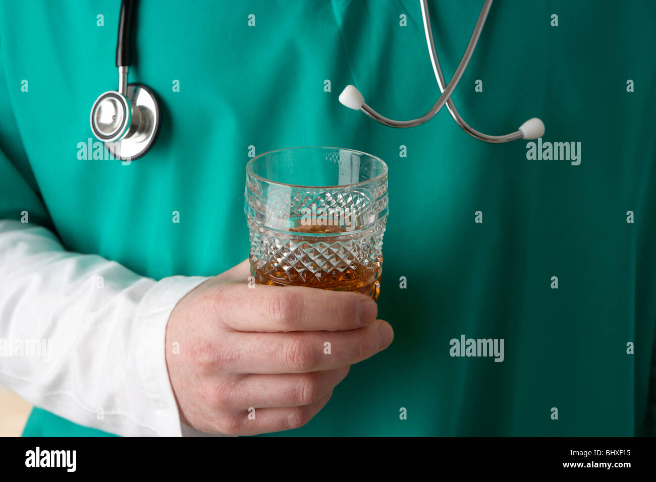 Uomo che indossa medical scrubs e stetoscopio tenendo un bicchiere di liquori alcol Foto Stock