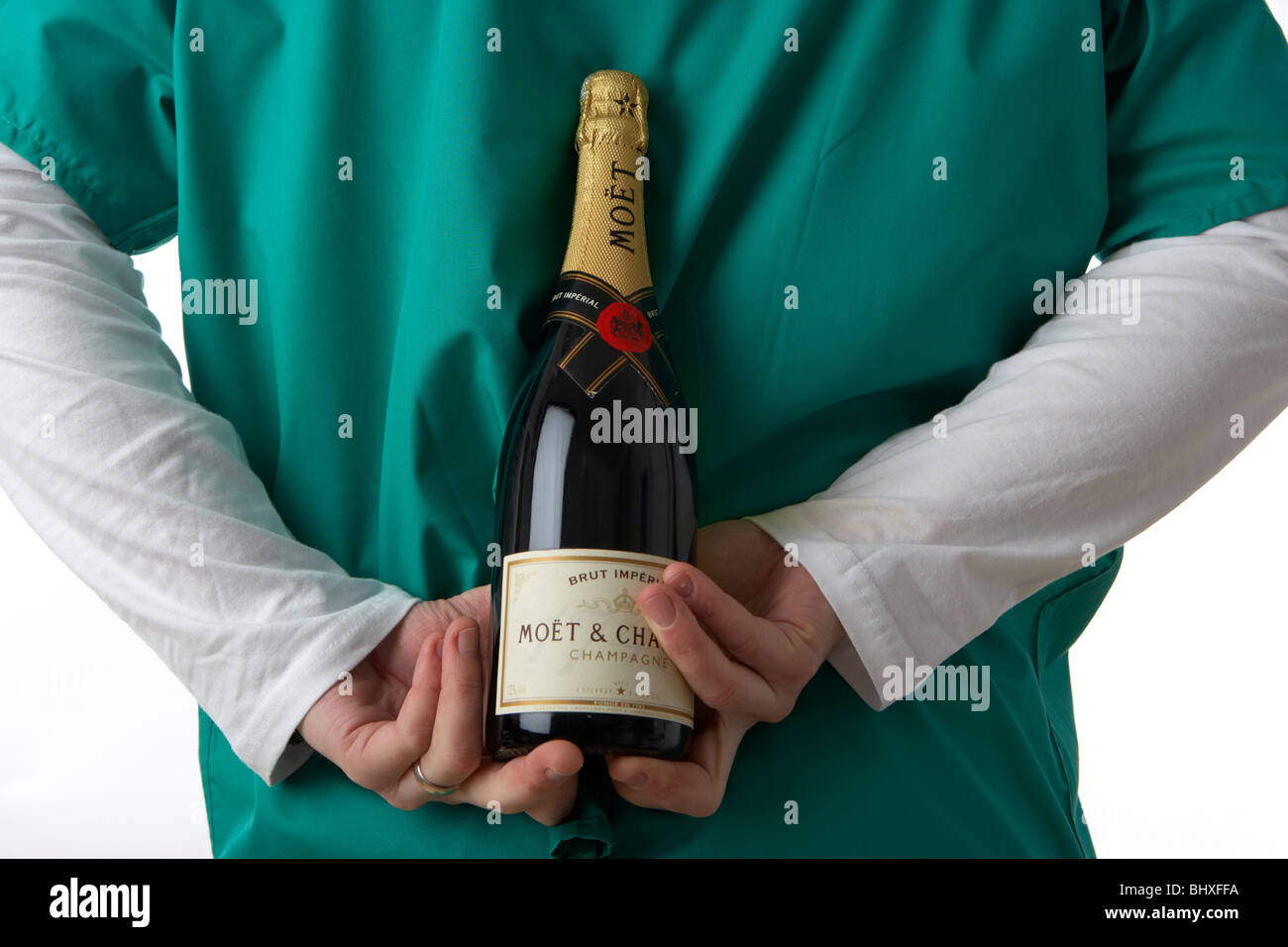 Uomo che indossa medical scrubs tenendo la bottiglia di champagne dietro la schiena Foto Stock