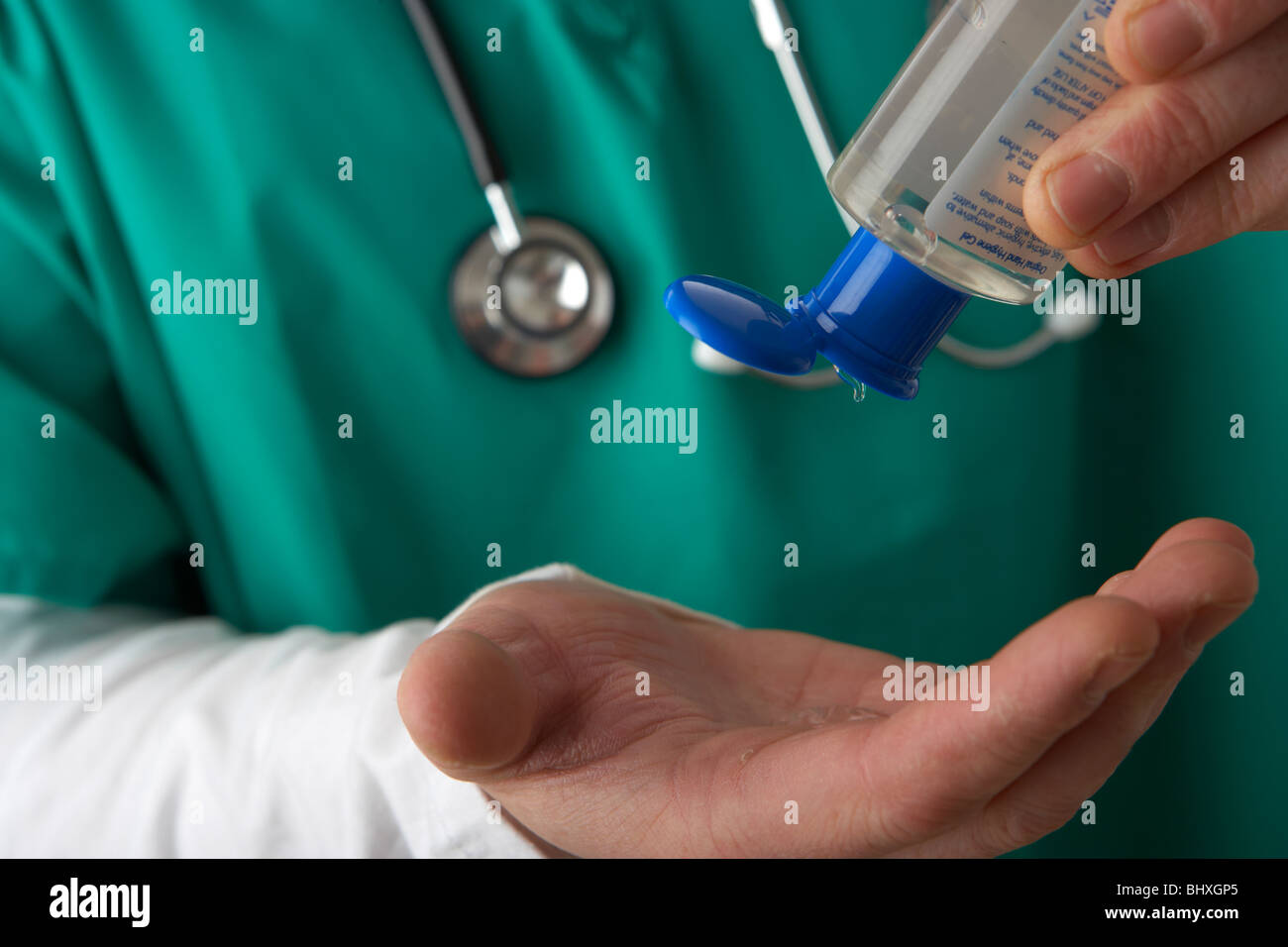 uomo che indossa scrub medici e stetoscopio versando l'igienizzatore per mani con gel alcolico da una bottiglia portatile nelle sue mani Foto Stock