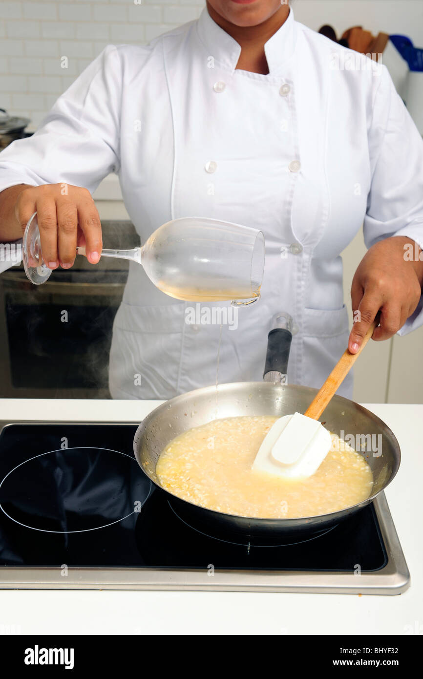 Lo chef cucinare il risotto versando il vino bianco nella padella, close-up Foto Stock