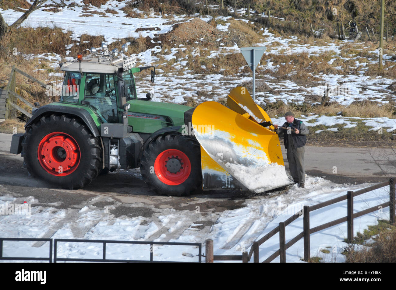 Un uomo di badili off neve congelate da un trattore spazzaneve / aratro. Foto Stock