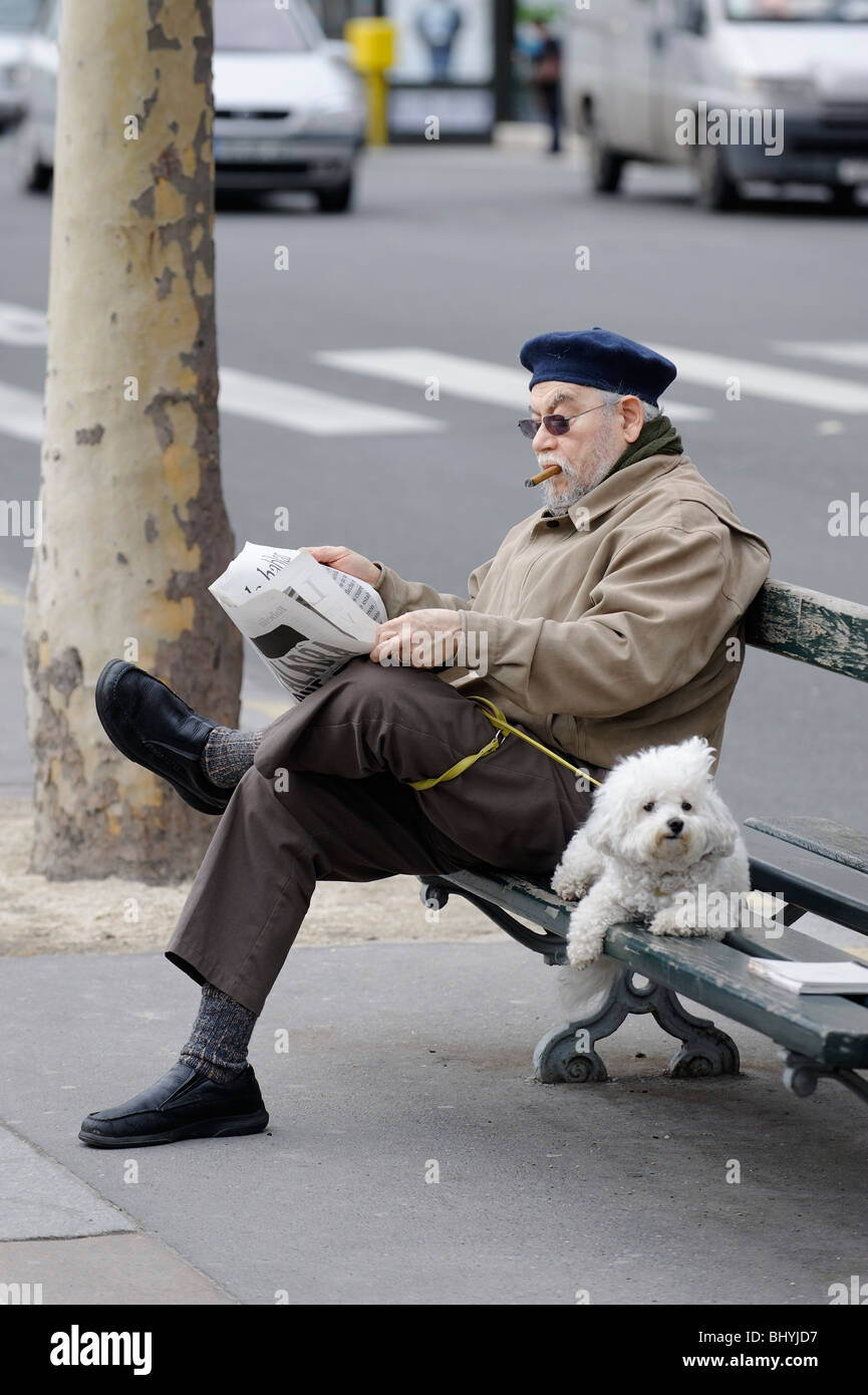 Un uomo in francese tradizionale beret e sigaro la lettura della carta con un cane in una strada di Parigi banco. Foto Stock