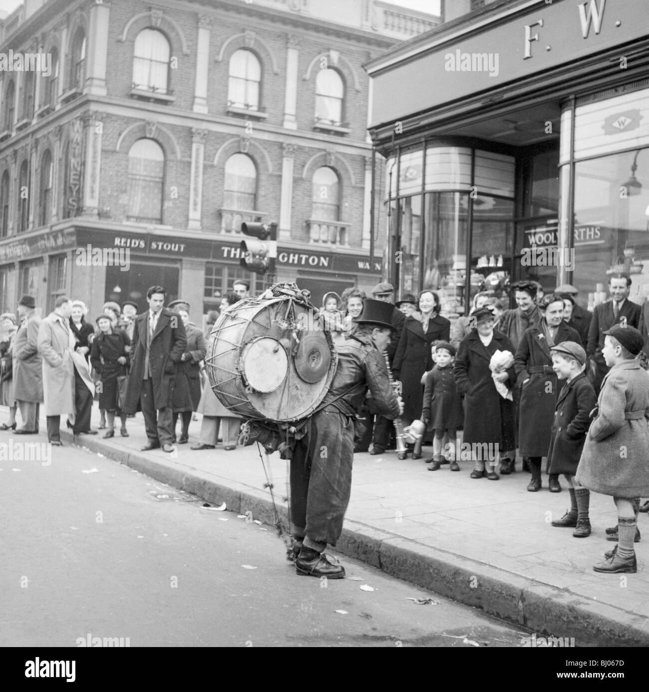 One-man band esibirsi di fronte ad una folla fuori Woolworths, Camden, London, 1952. Artista: Henry Grant Foto Stock