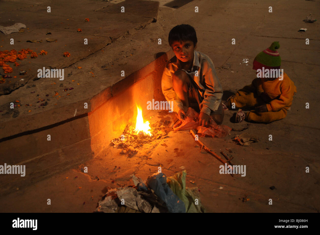 Due bambini piccoli incendi di luce da sacchetti di plastica per mantenere in caldo su uno di Varanasi's Ghats in India Foto Stock