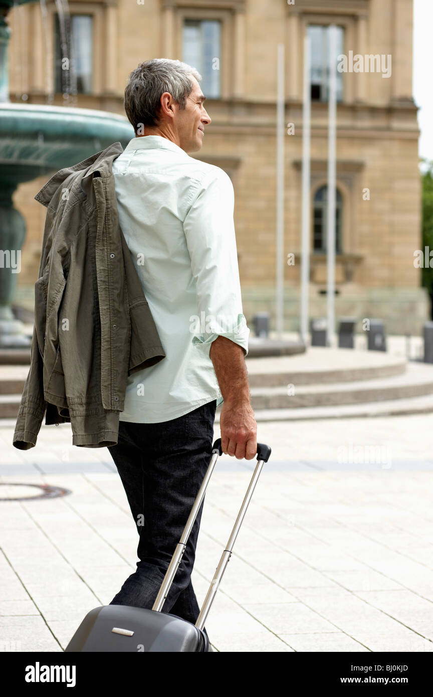 Uomo che cammina attraverso la strada di città tirando carry-in Foto Stock