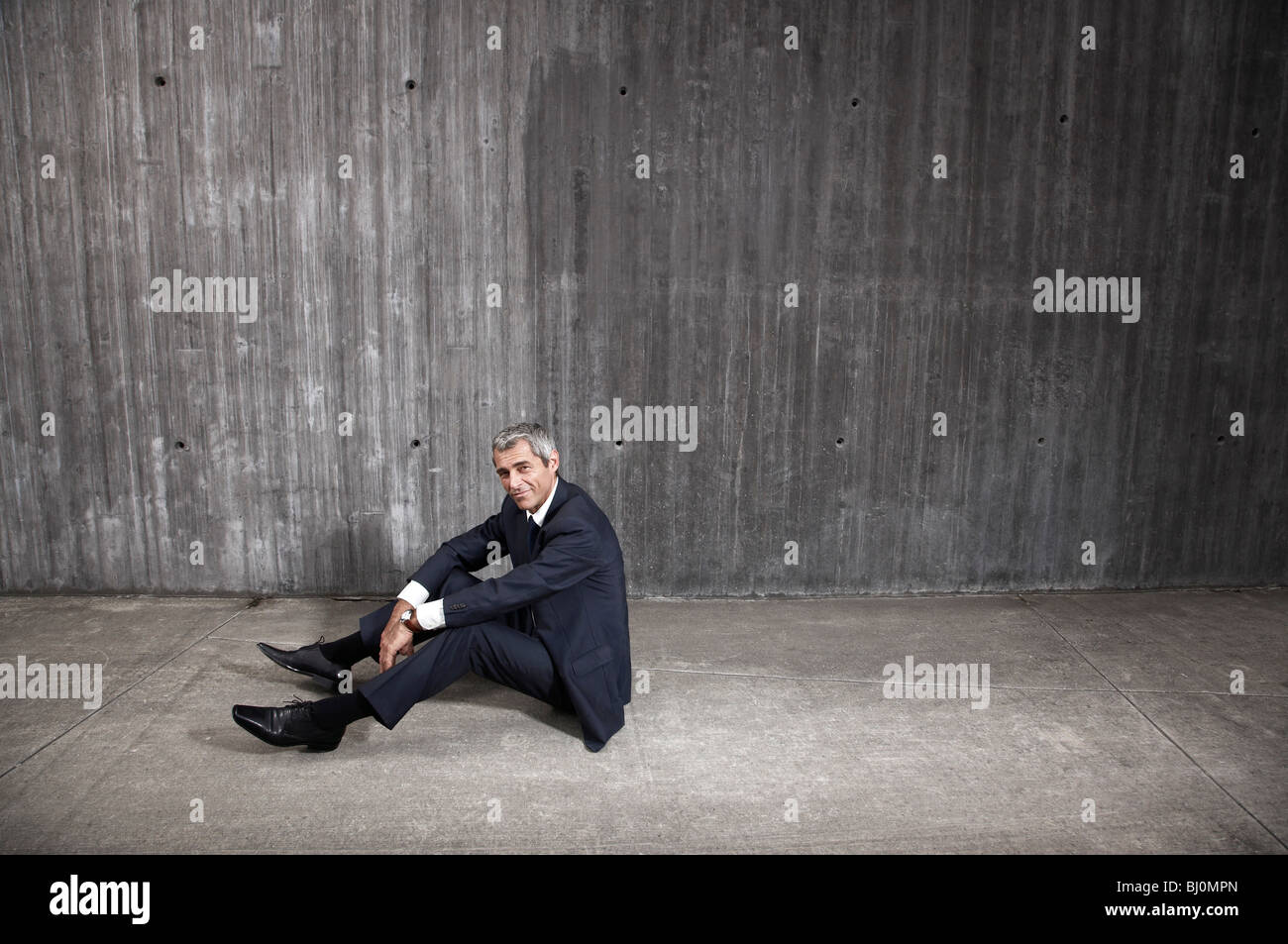 Imprenditore seduto sul pavimento nella parte anteriore del muro di cemento Foto Stock