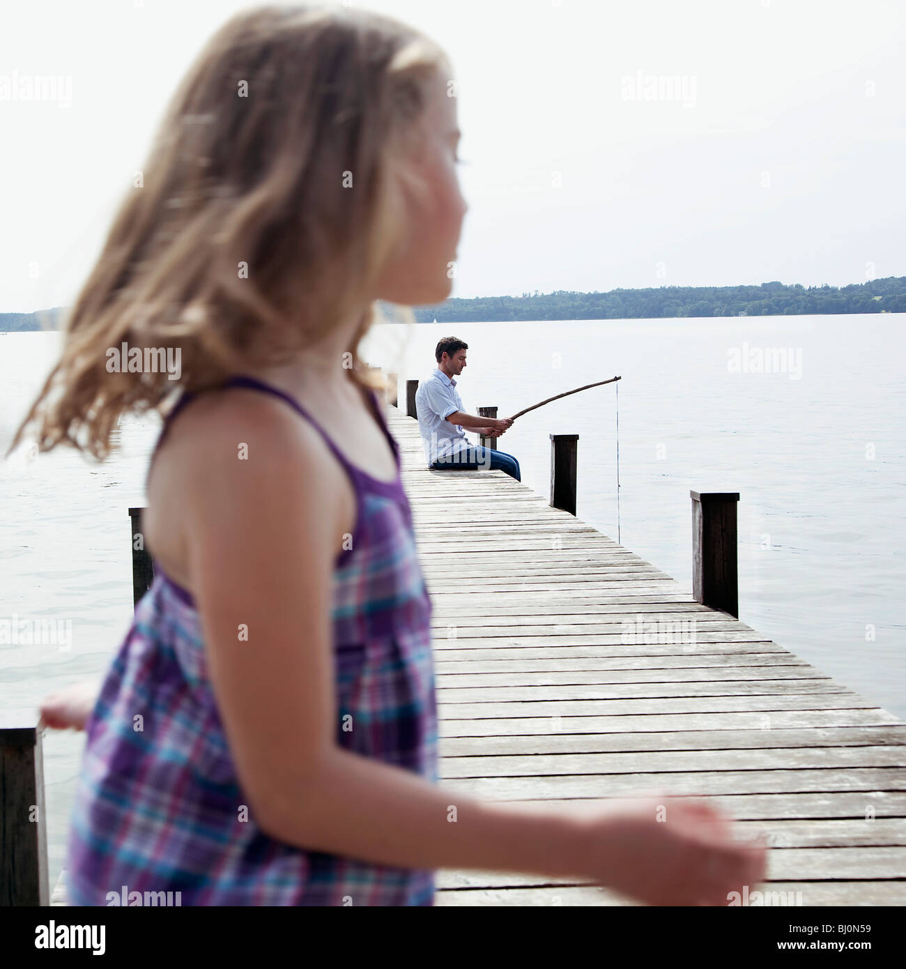 L'uomo angling sul molo con la giovane figlia in primo piano Foto Stock