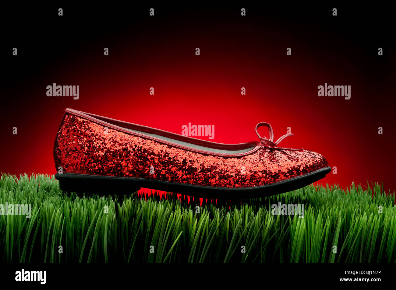 Sequined rosso pantofola su erba verde contro un affievolimento sfondo rosso Foto Stock