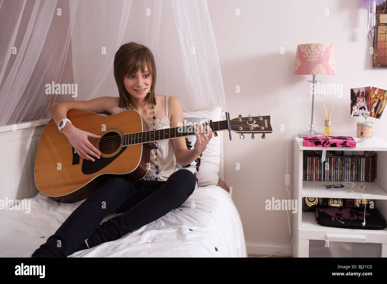Ragazza adolescente 14 suonare una chitarra acustica sul suo letto Foto Stock