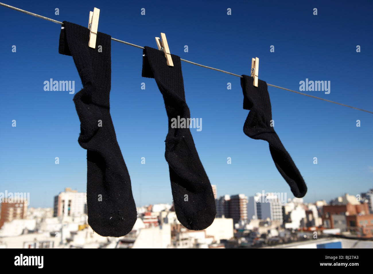 Coppia di calze nere e un tipo strano appeso su una linea di lavaggio con cielo blu su una skyline della città Foto Stock