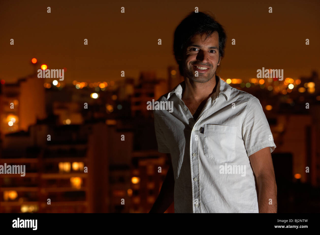 Ispanico uomo latino permanente sulla terrazza sul tetto con sorridente serale città in background in buenos aires argentina Foto Stock