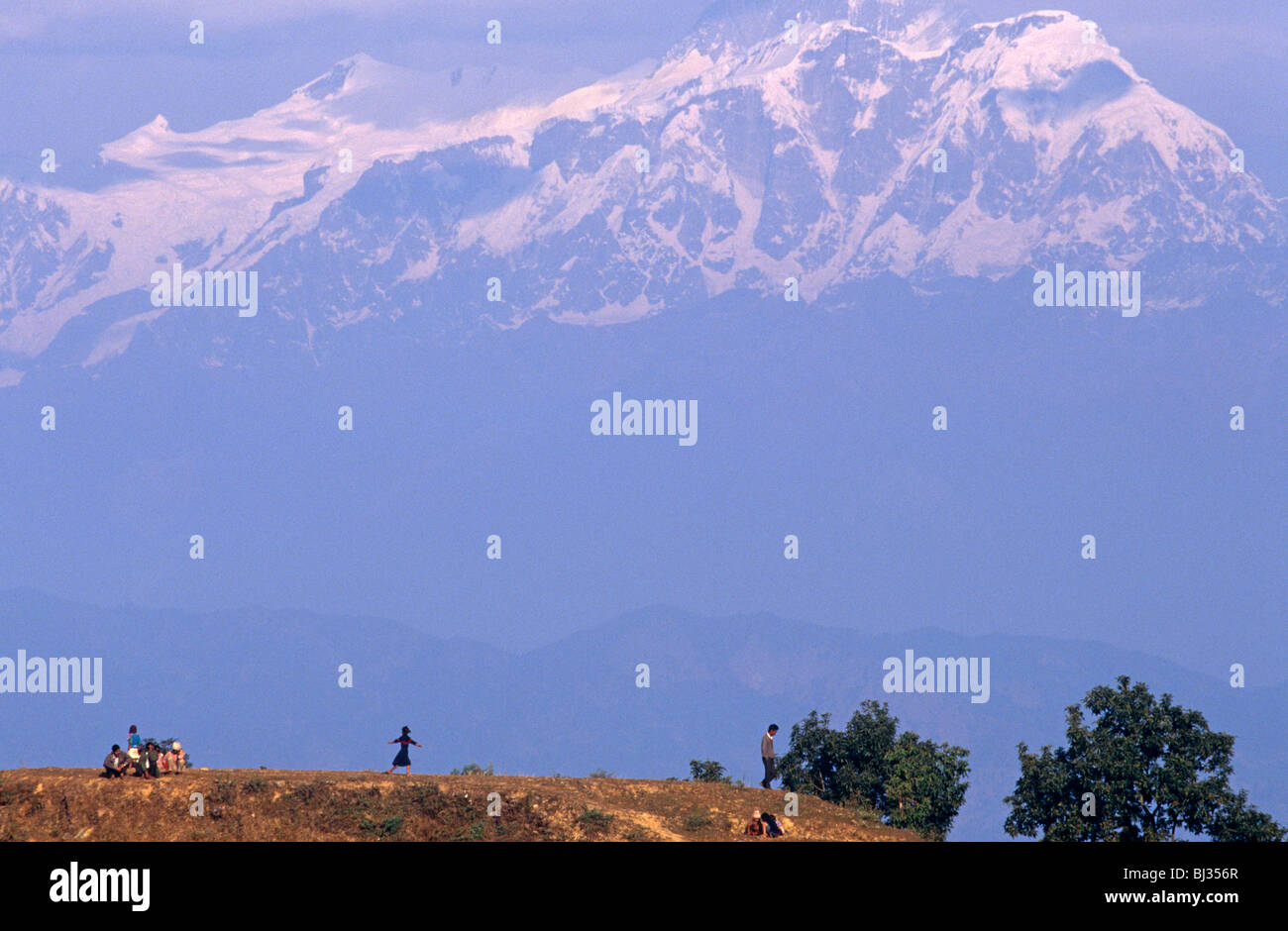 Con un fondale Himalayana, una famiglia Nepalese crouch sulla cima della collina di riposo durante una bella passeggiata in famiglia dalla loro comunità villaggio. Foto Stock