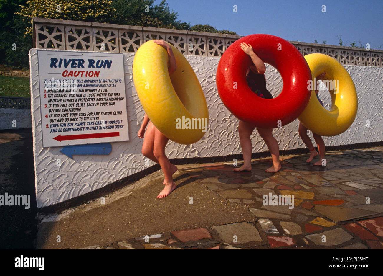 Goffamente che trasportano i loro gigante gli anelli in gomma avvolgendo le loro mani a sinistra sopra la parte superiore di curve, tre bambini portare acqua ride anelli Foto Stock