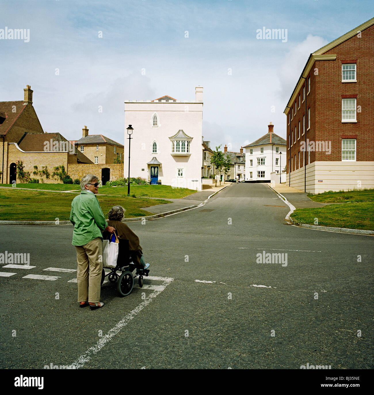 Una strana prospettiva di alloggiamento deserte e strade vuote, Jen West e gli anziani in sedia a rotelle madre Margaret in Poundbury. Foto Stock