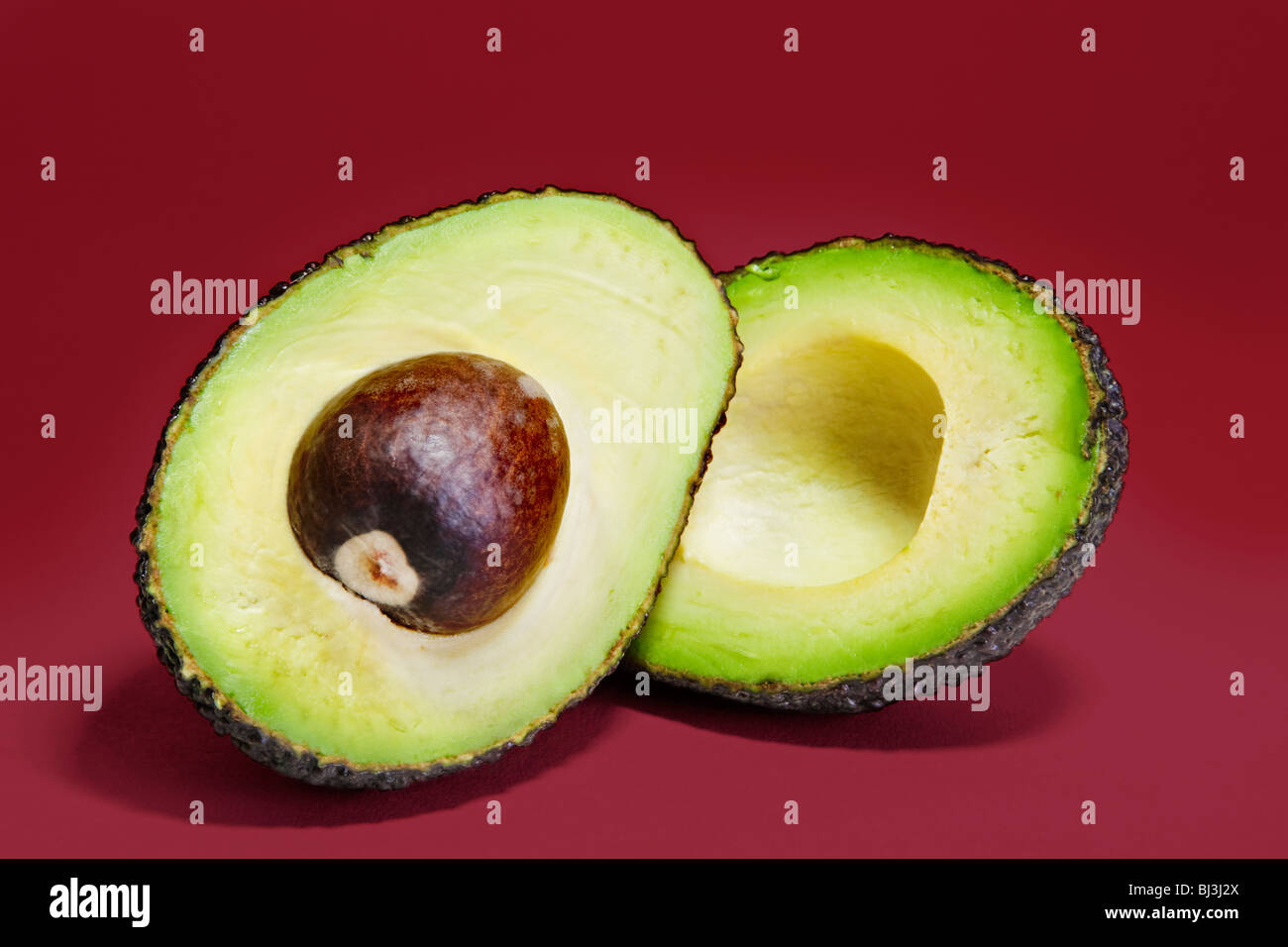 Varietà Hass avocado pera tagliata in due metà contro uno sfondo di colore rosso. Foto Stock