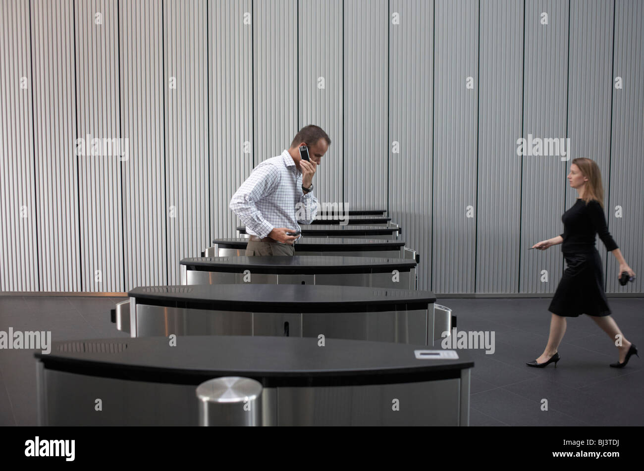 Estensione con fiducia una femmina di dipendente di una società internazionale fa il suo cammino verso la barriera di sicurezza come un collega esce. Foto Stock