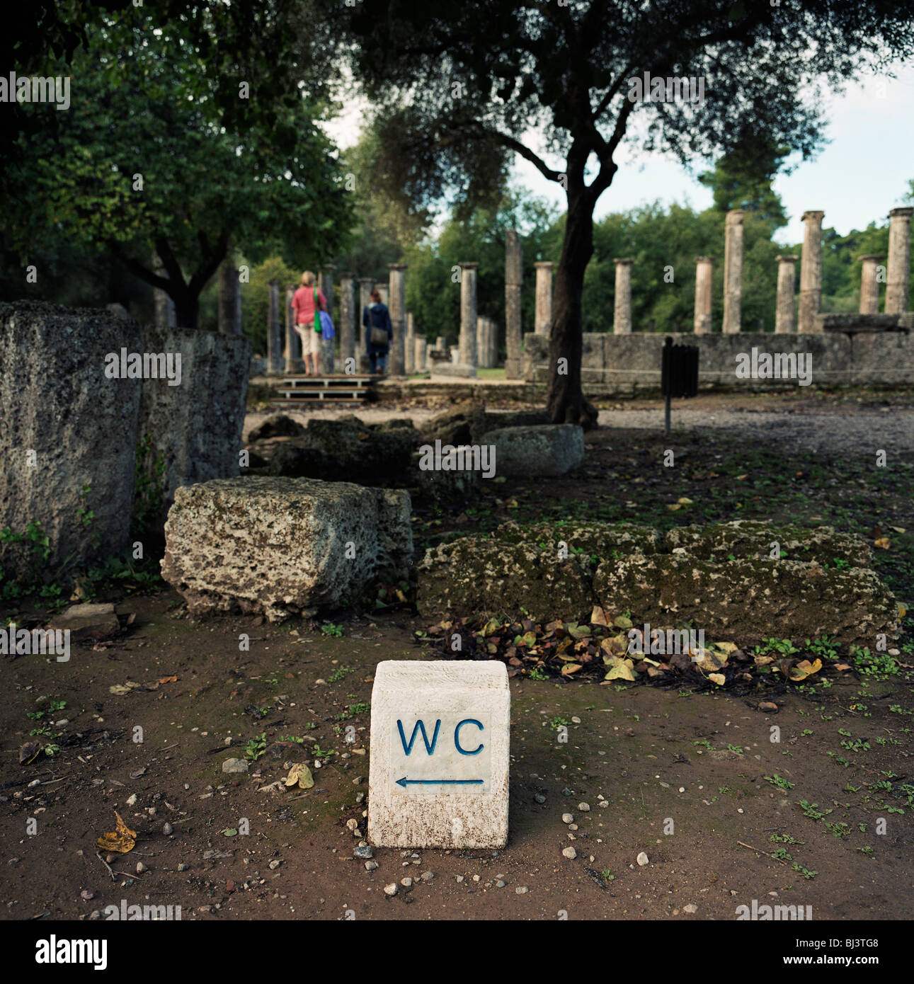 Un wc segno si siede vicino alla permanente di colonne doriche e turisti a Olimpia antica's Palaestra o scuola di wrestling. Foto Stock