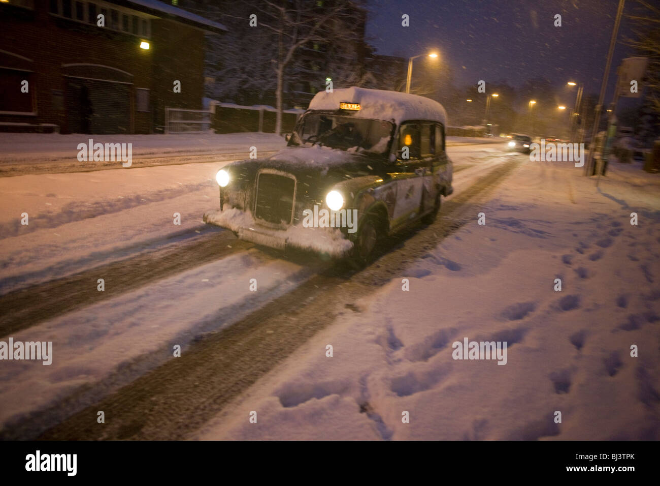Un brave taxi cab driver rigidi con circospezione lungo Denmark Hill nel sud di Londra durante il mattino nevicate. Foto Stock