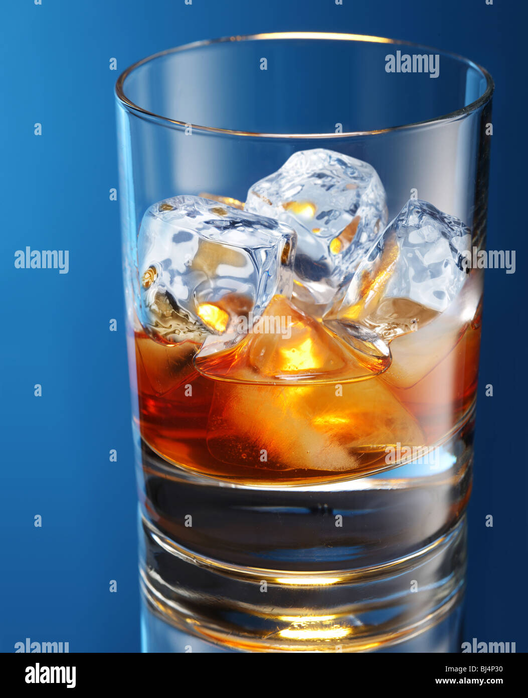 Bicchiere di brandy con cubetti di ghiaccio isolato su un blu Foto Stock
