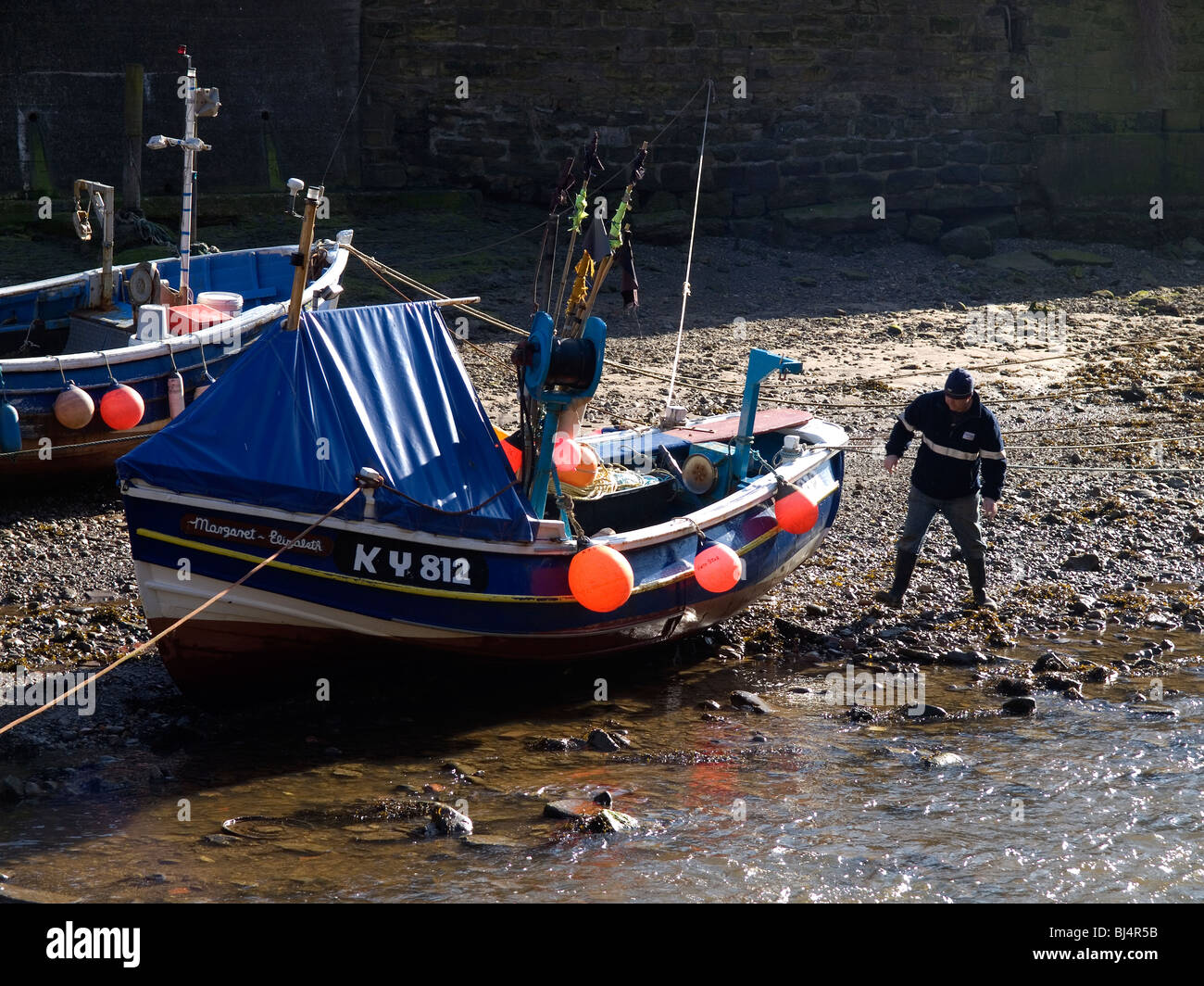 Un pescatore costiero controllando la sua barca su Roxby Beck Staithes North Yorkshire Foto Stock