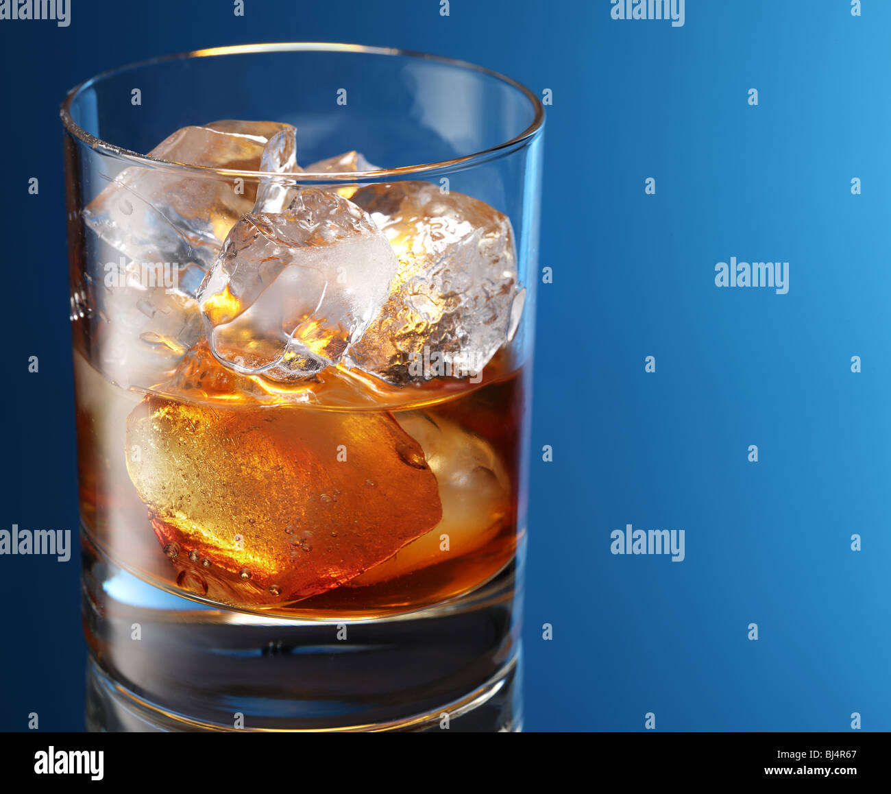 Bicchiere di brandy con cubetti di ghiaccio isolato su un blu Foto Stock