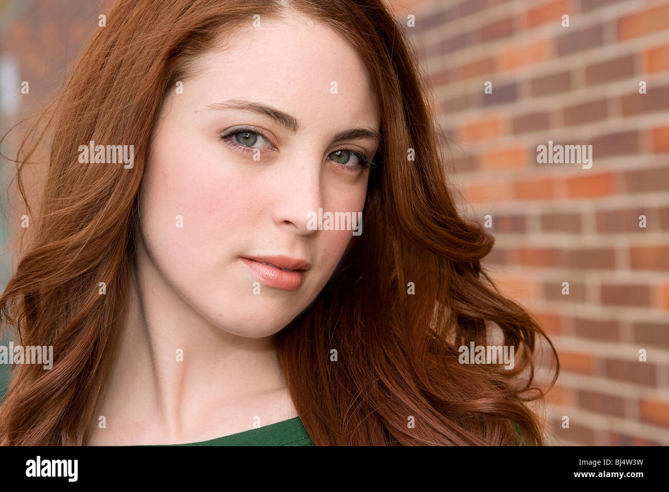 Closeup headshot ritratto di un attraente ventenne giovane donna rossa accanto a un muro di mattoni Foto Stock