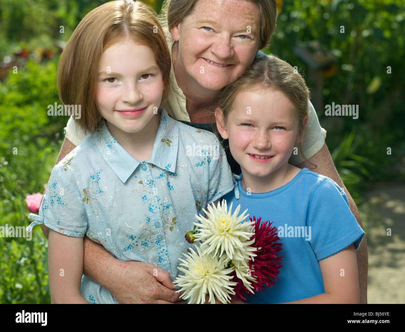 Una donna che abbraccia due ragazze in un giardino Foto Stock