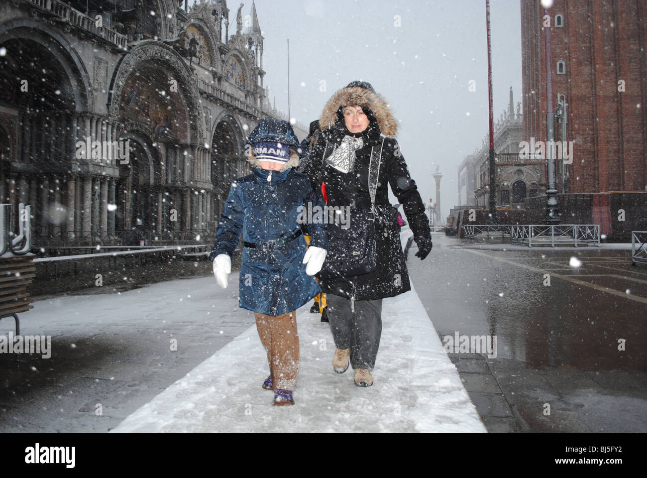 La gente a piedi lungo una passerella di ghiaccio in una tempesta di neve, di fronte alla Basilica di San Marco, Piazza San Marco, Venezia, Italia Foto Stock