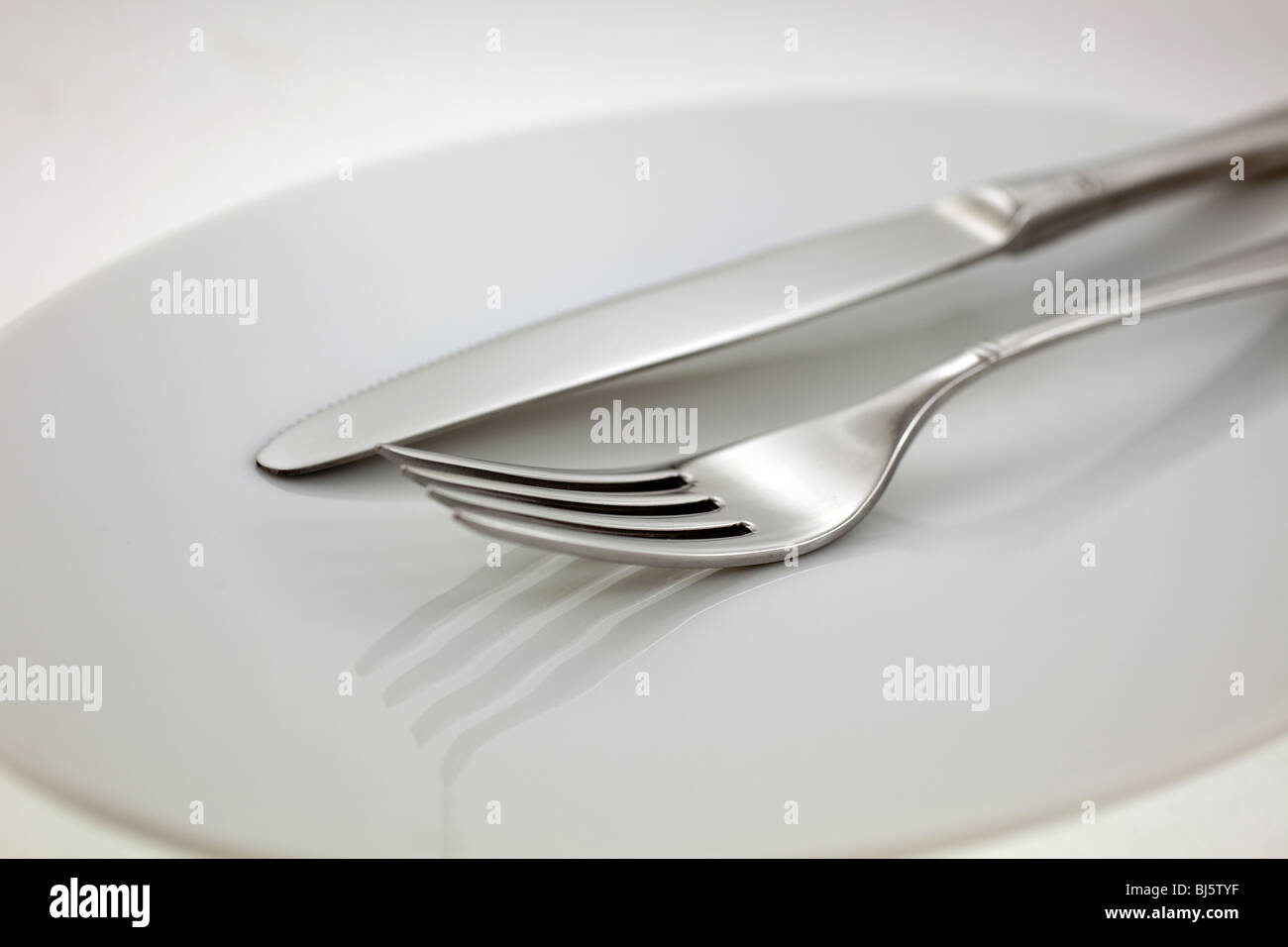 Posate in acciaio: forchetta e coltello su una piastra bianca Foto Stock