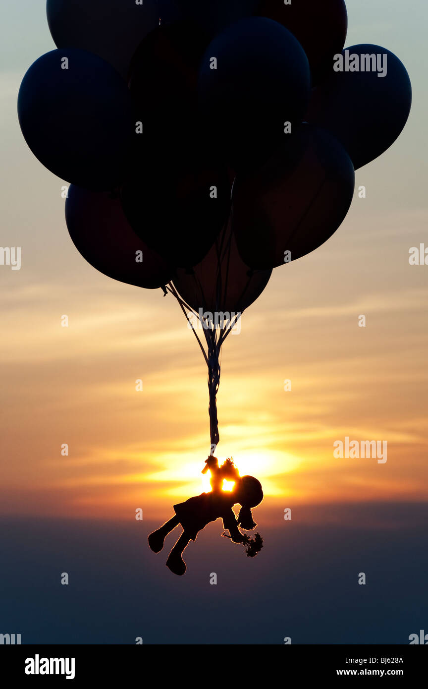 Rag Doll tenuta su palloni di elio che si allontanano al tramonto. Silhouette Foto Stock