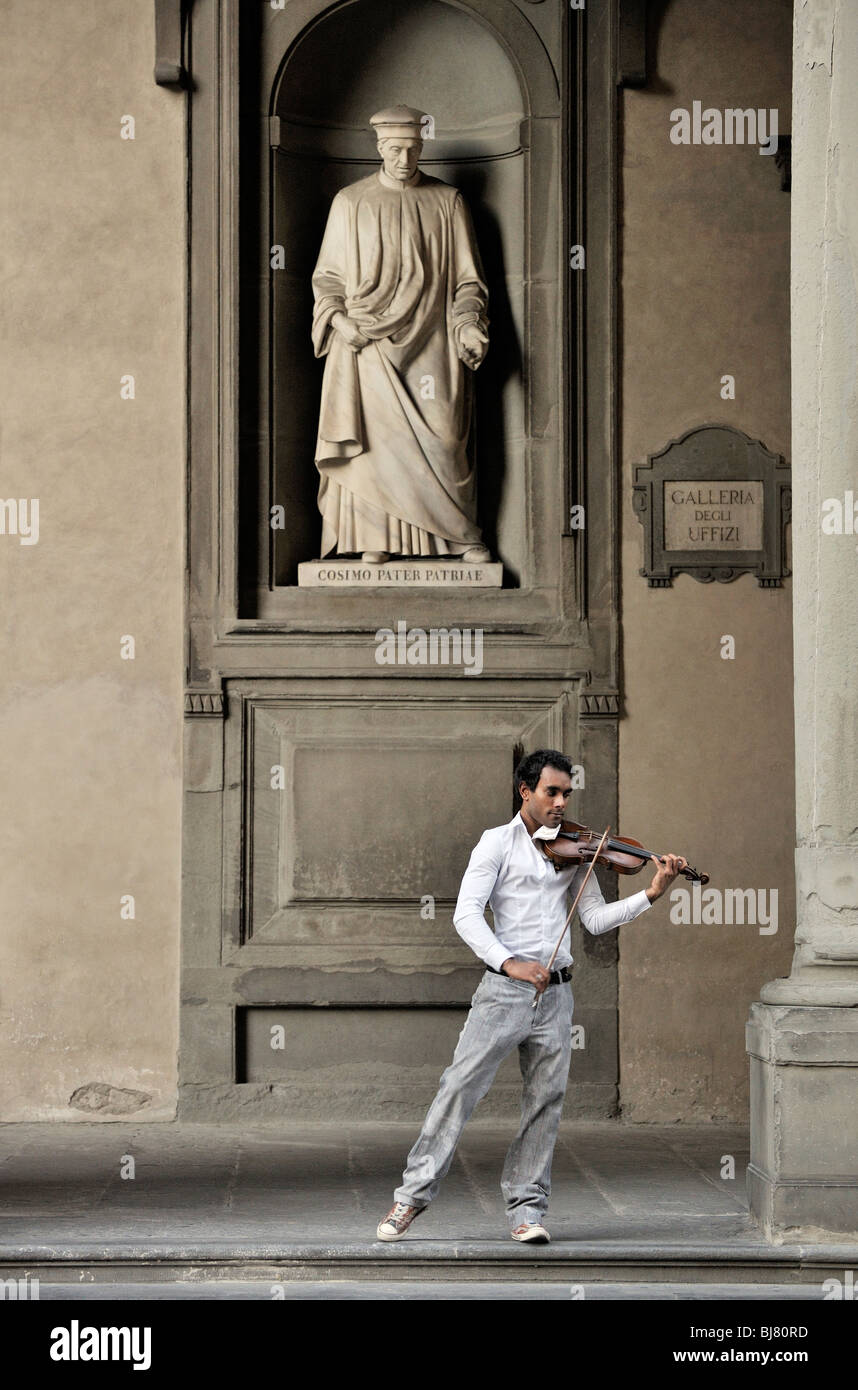 Firenze, Italia. Musicista di strada suona violino classico sotto la statua della città padre Cosimo de' Medici. Al di fuori della Galleria degli Uffizi Foto Stock
