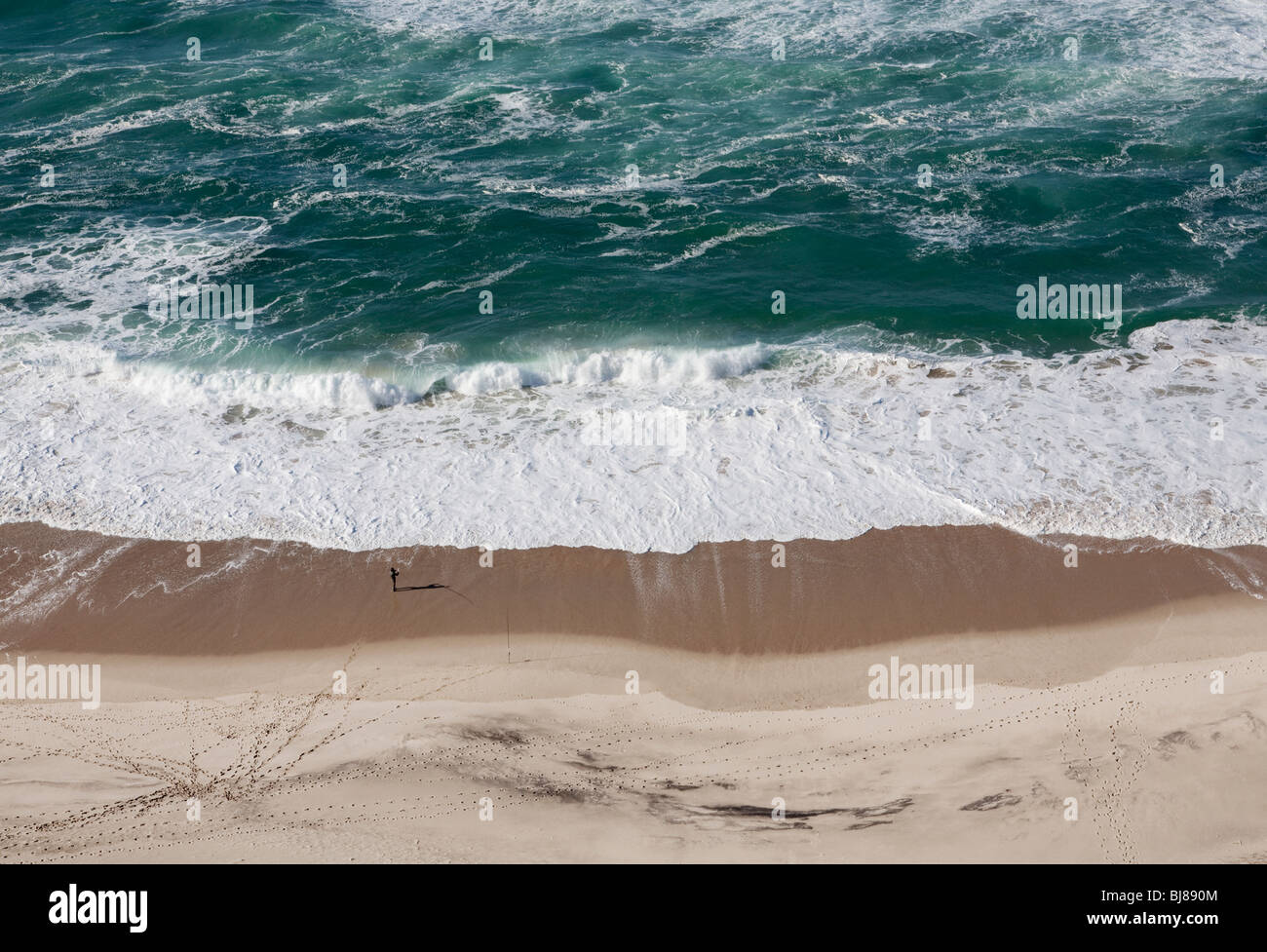 Una piccola persona in piedi su una grande spiaggia di sabbia a guardare l'oceano shot dal di sopra Foto Stock