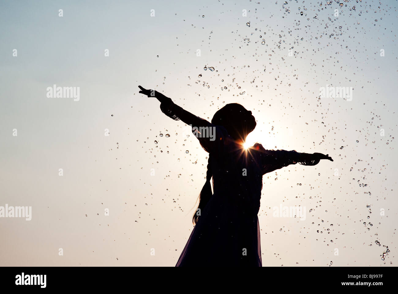 Silhouette di una giovane ragazza indiana godendo di essere spruzzato con acqua. India Foto Stock